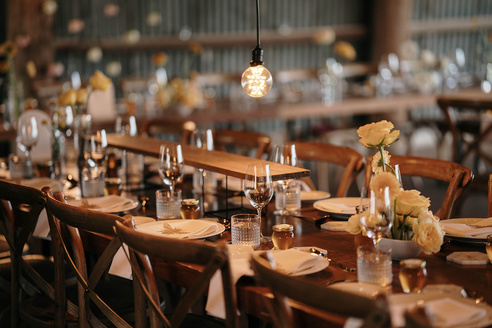 Dark Wood Wedding reception tables laid with glassware, plates, napkins, rosie's lasercut bee place settings and flowers
