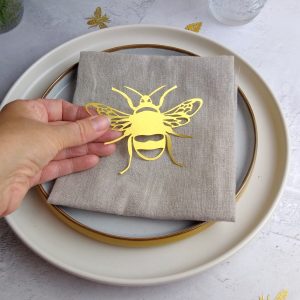 Gold Lasercut Paper Bumble Bee Place Setting held in model's hand above beige linen napkin on yellow edged cream plates.