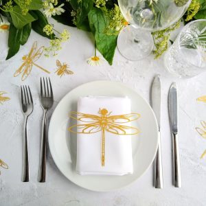 Gold lasercut Dragonlfy place setting sits on top of white linen napkin on a table decorated for a wedding.