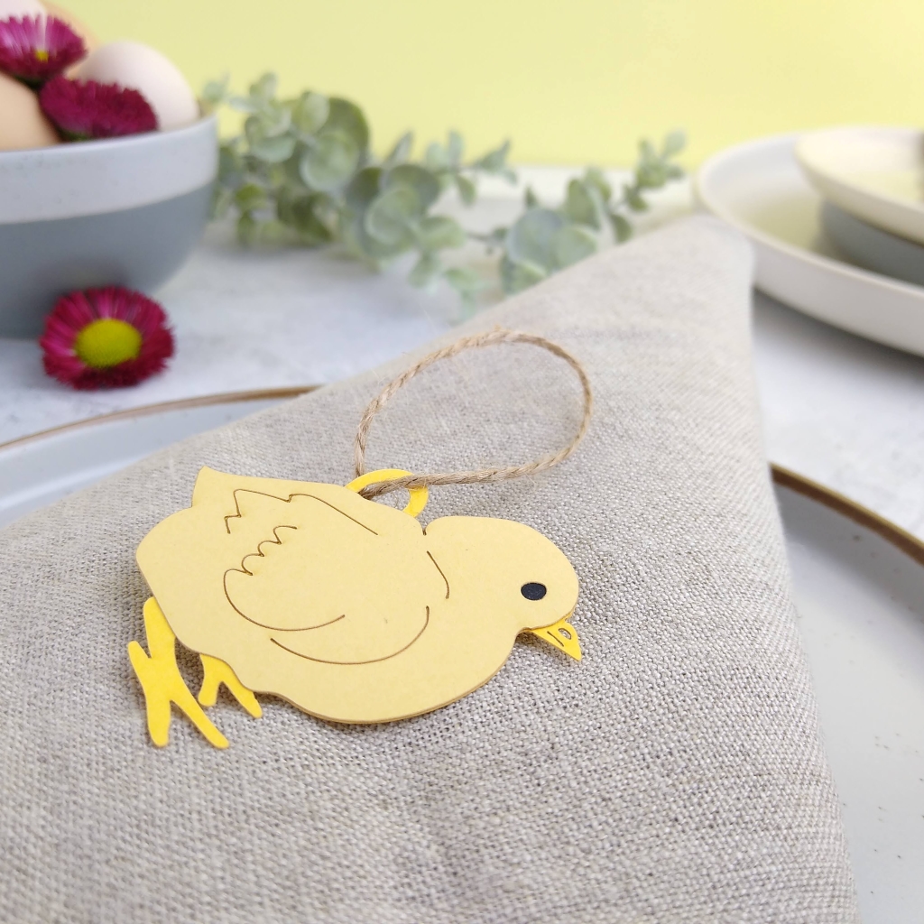Paper Easter Chick with hanging loop placed on beige linen napkin as a place setting.