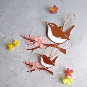 Large and small wren papercut hanging decorations. Brown and white wrens sit on brown branch with blossom. Blossom is pale pink with dark pink edges.
