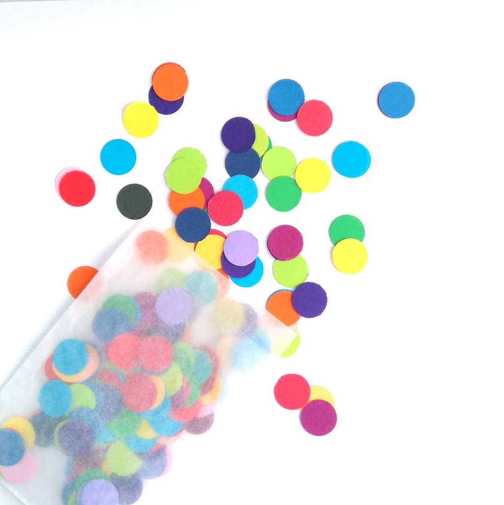 Rainbow Dot Party Confetti spills out of glassine bag onto white table.