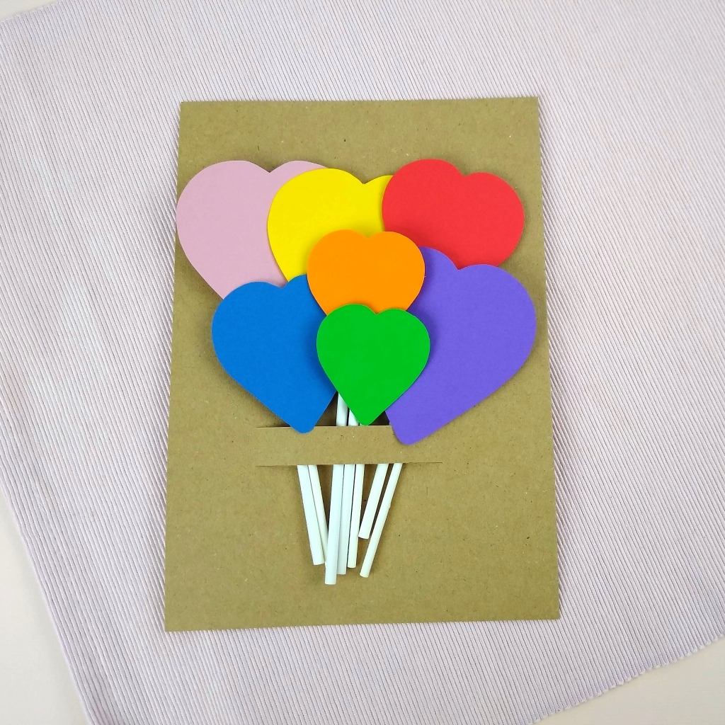 Set of 7 heart cake topper decorations are packaged on a cardboard backing sheet. Decorations are held in place by the sticks being fed through a slit in the backing sheet.