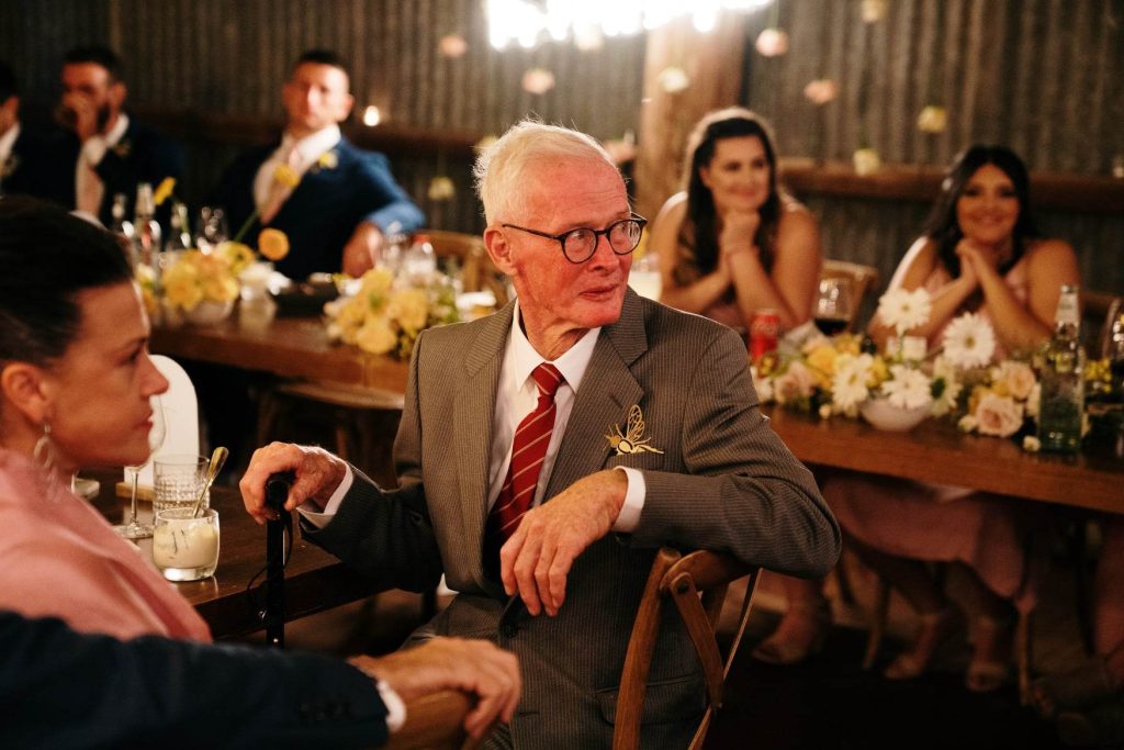 Bride's Grandfather "Pappy" seated at wedding reception. He is wearing Rosie's lasercut honeybee decoration in his suit pocket