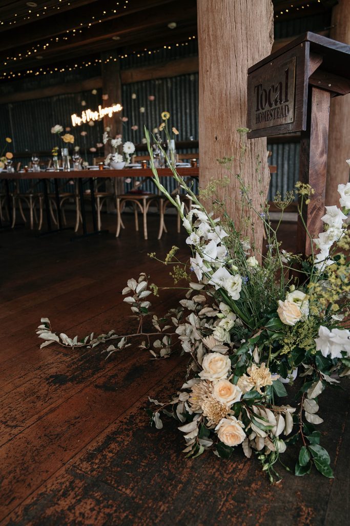 Flower arrangement featuring gladiloli and roses placed on floor in front of wooden pillar