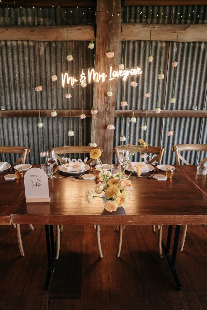 Mr and Mrs Lovegrove written in neon lights displayed behind bride and grooms place at the top table. Cream roses are hung from wires to create a floral backdrop