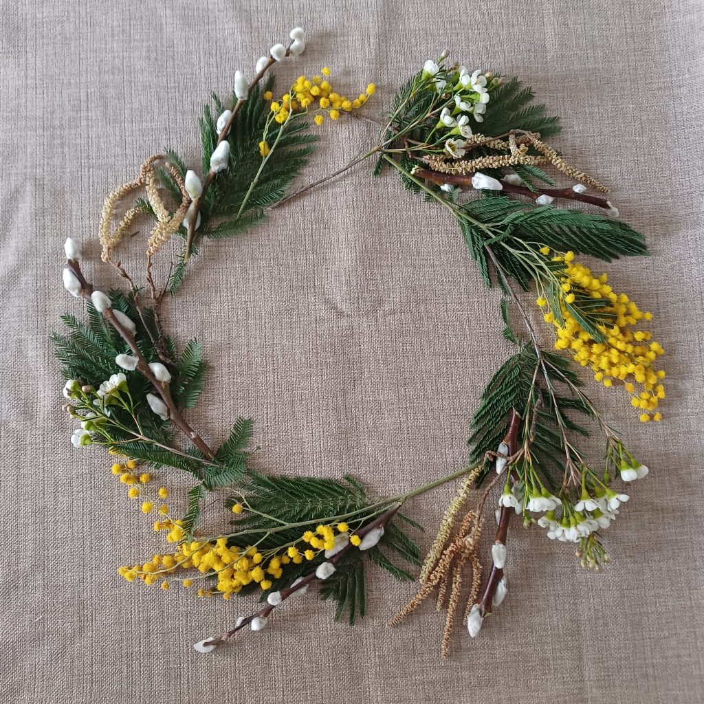 "Wreath" created from mimosa, catkins, waxflower and pussy willow laid on a taupe linen table cloth.
