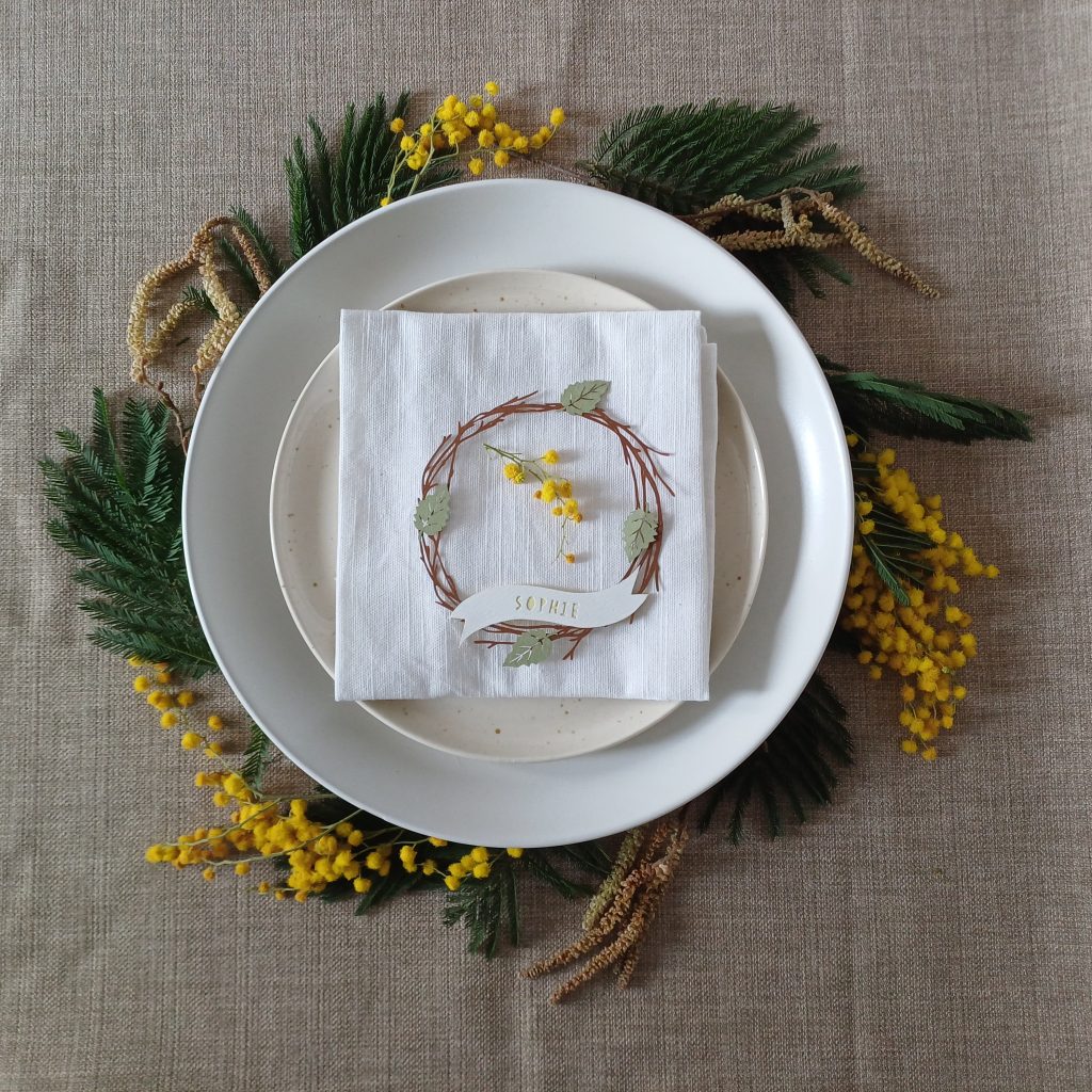 Sprigs of mimosa flowers and foliage, along with catkins placed under the edge of layered plates to create a wreath effect.