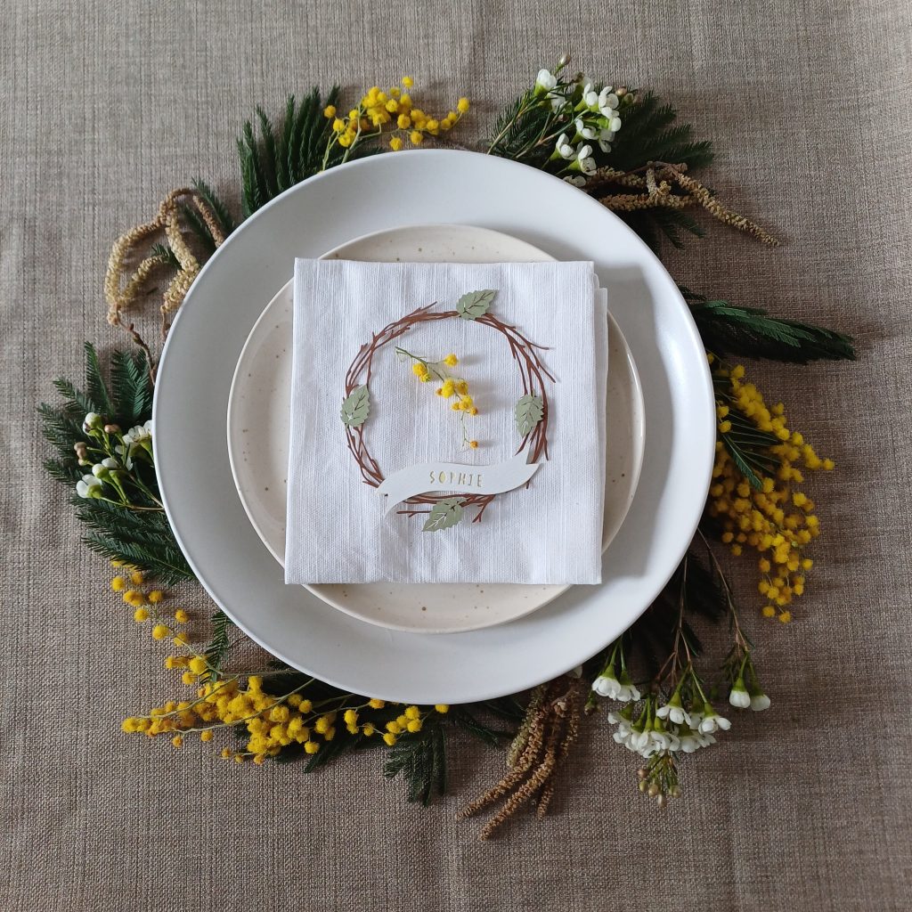 Sprigs of mimosa, catkins and waxflower placed under the edge of layered plates to create a full wreath effect