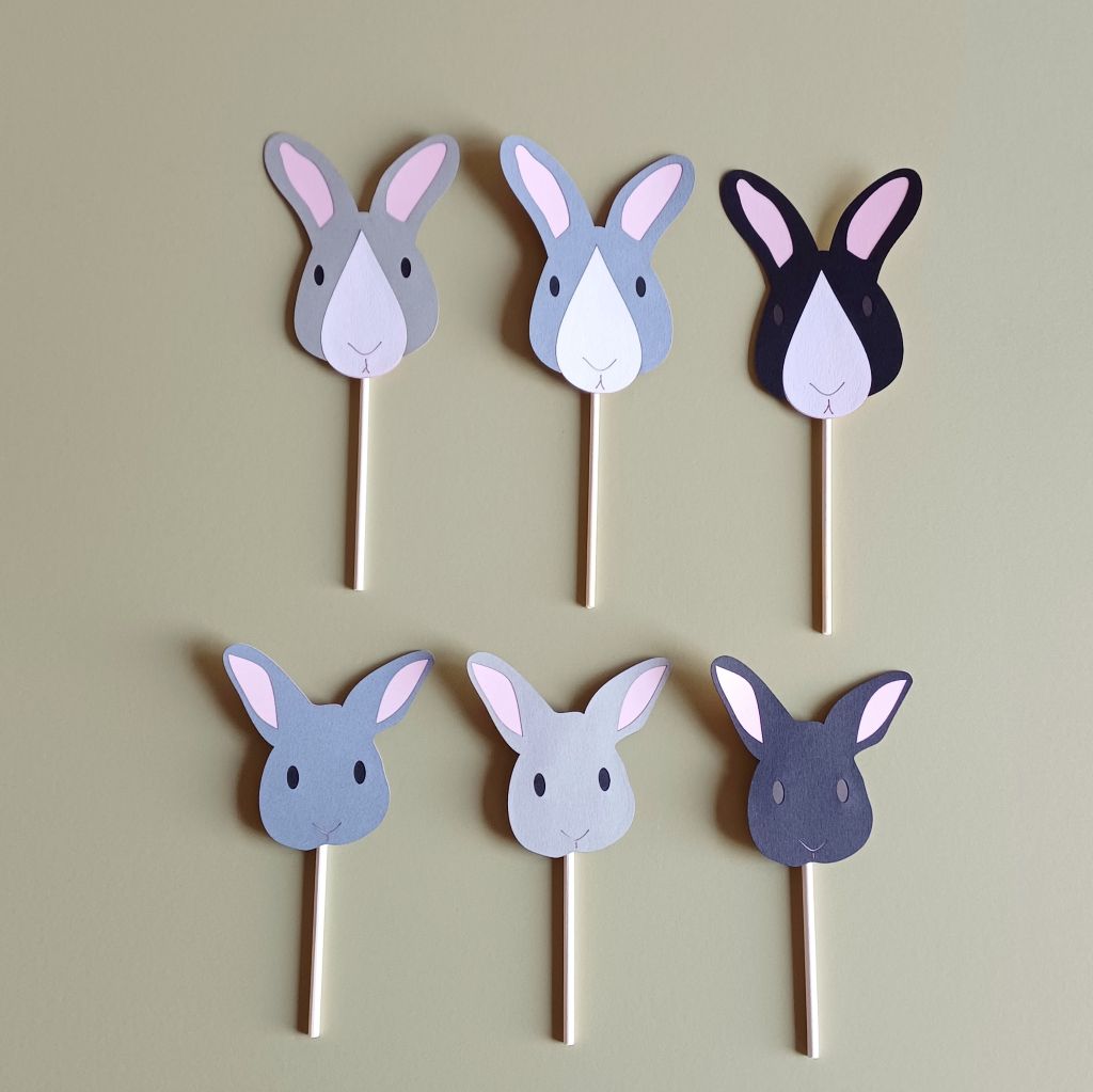 Grey, black and white bunny cake topper option. Top row: 3 bunny cake toppers (left to right) Pale grey and Dark Grey rabbits with black eyes, a Black rabbit with dark brown eyes, all three rabbits have pale pink ears and a white nose patch. Bottom row (left to right) dark grey, pale grey bunnies with black eyes and a black bunny with dark brown eyes. All bunnies have pale pink ears and line details for nose and mouth. Each cake topper is attached to a white paper cake-pop stick