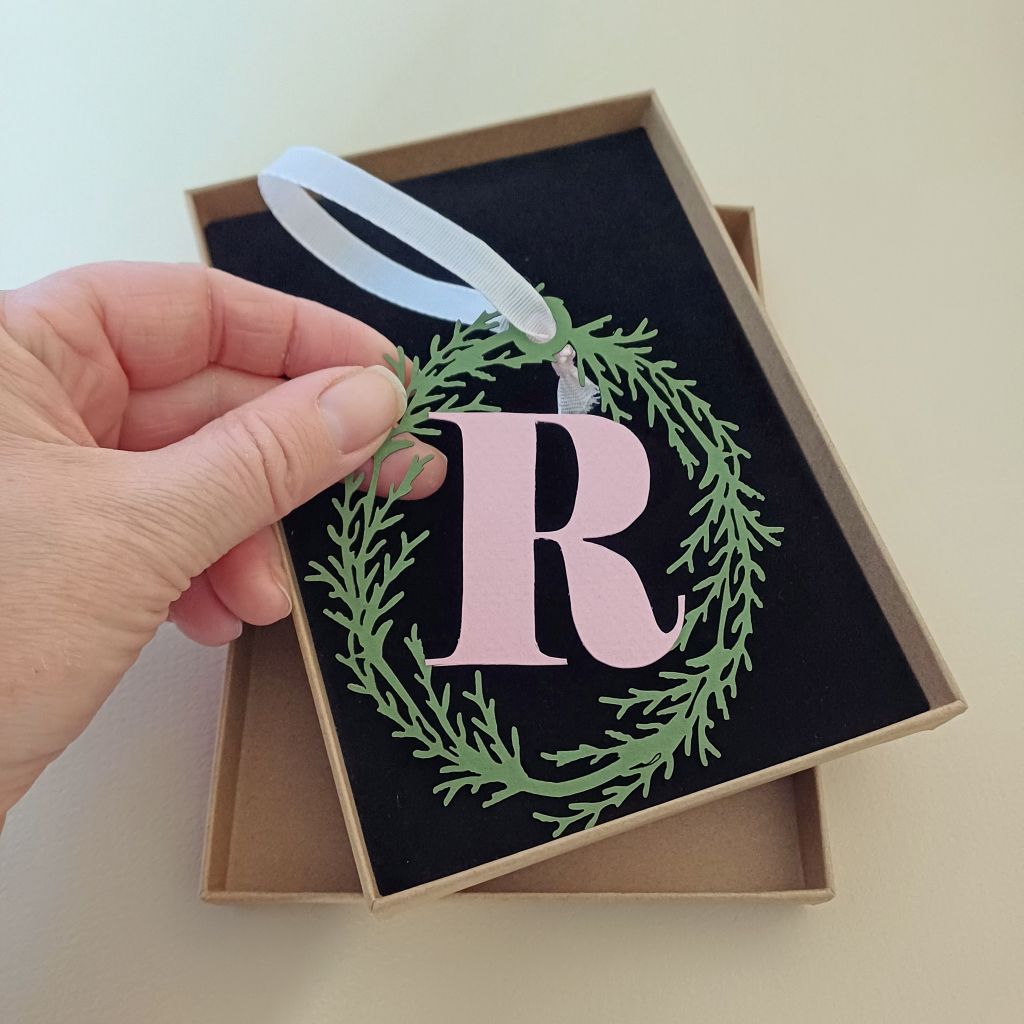 Papercut Hanging Decoration "R" in pale pink held in model's hand above cardboard presentation box